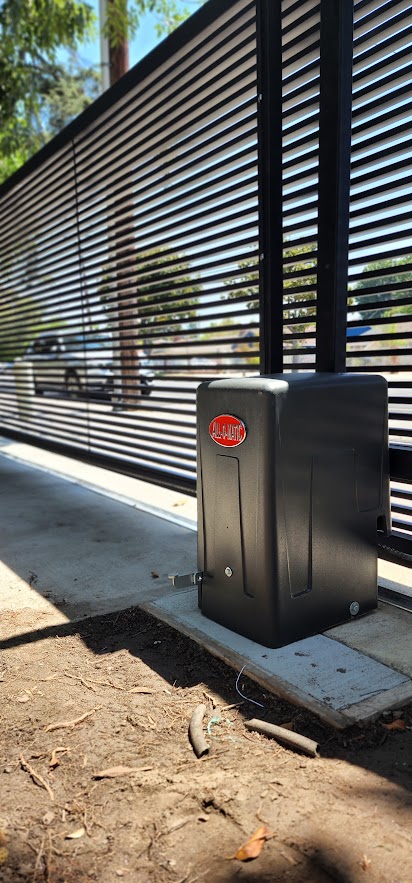 All-O-Matic slide gate operator in a black housing standing beside a horizontal slat sliding gate