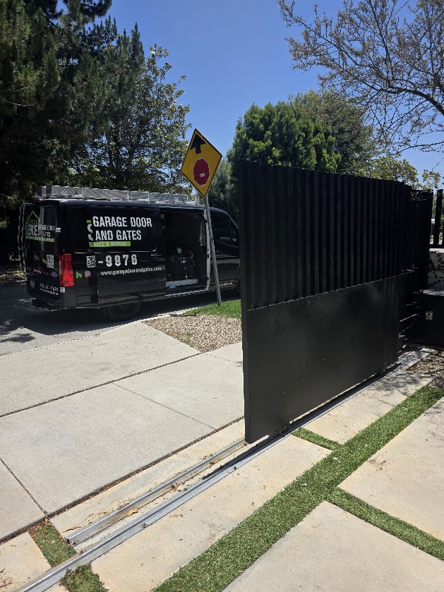 The repaired dark slatted sliding gate closed and running on its track, with the service van parked at the kerb