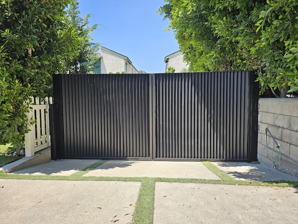 Dark double swing driveway gate with vertical corrugated steel panels, closed across a concrete driveway
