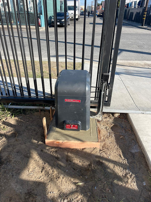 LiftMaster SL3000UL slide gate operator with its cover on, mounted on a concrete pad beside a wrought iron gate