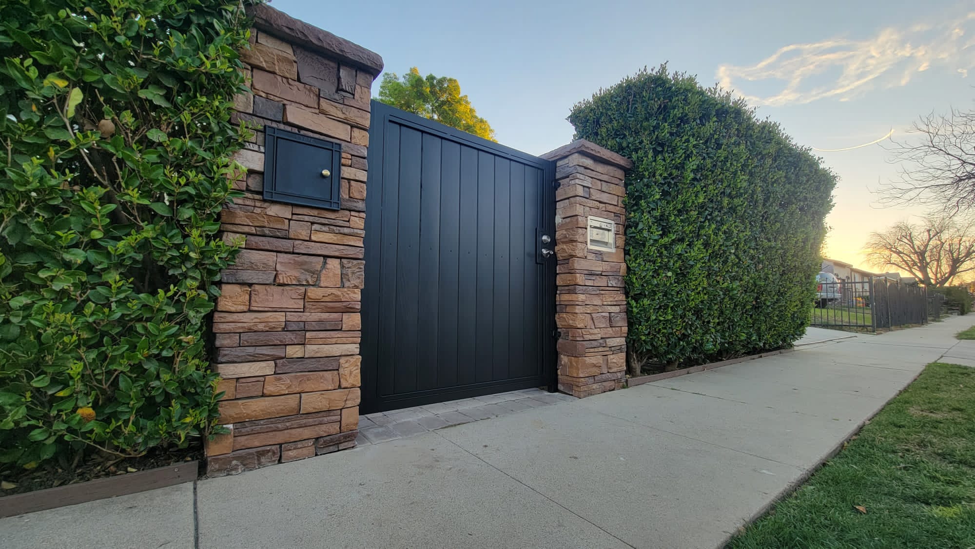 Metal-frame vertical wood tongue-and-groove full-privacy gate, two stone pillars. Encino.