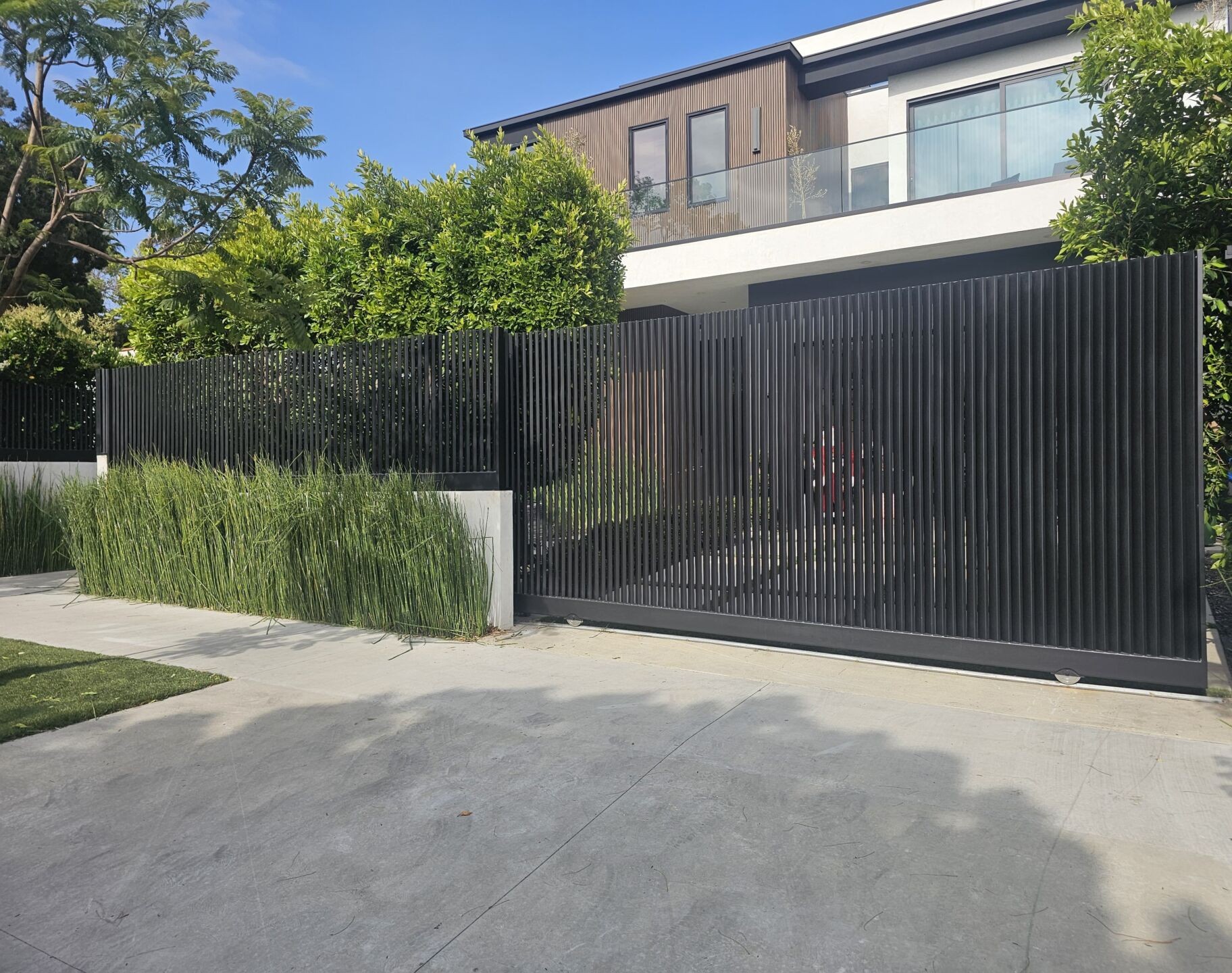 Sliding driveway gate with vertical-slot infill beside matching slat fencing at a West Hollywood residence