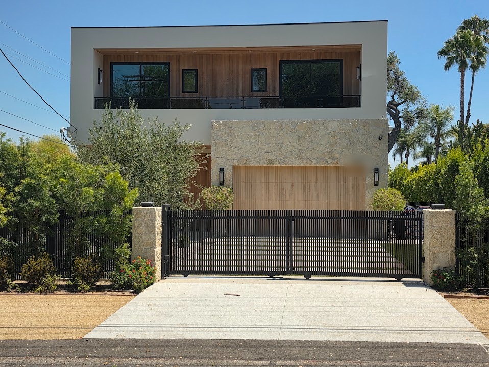 Double sliding driveway gate with stone-faced columns and a white oak vertical-slot garage door at an Encino residence