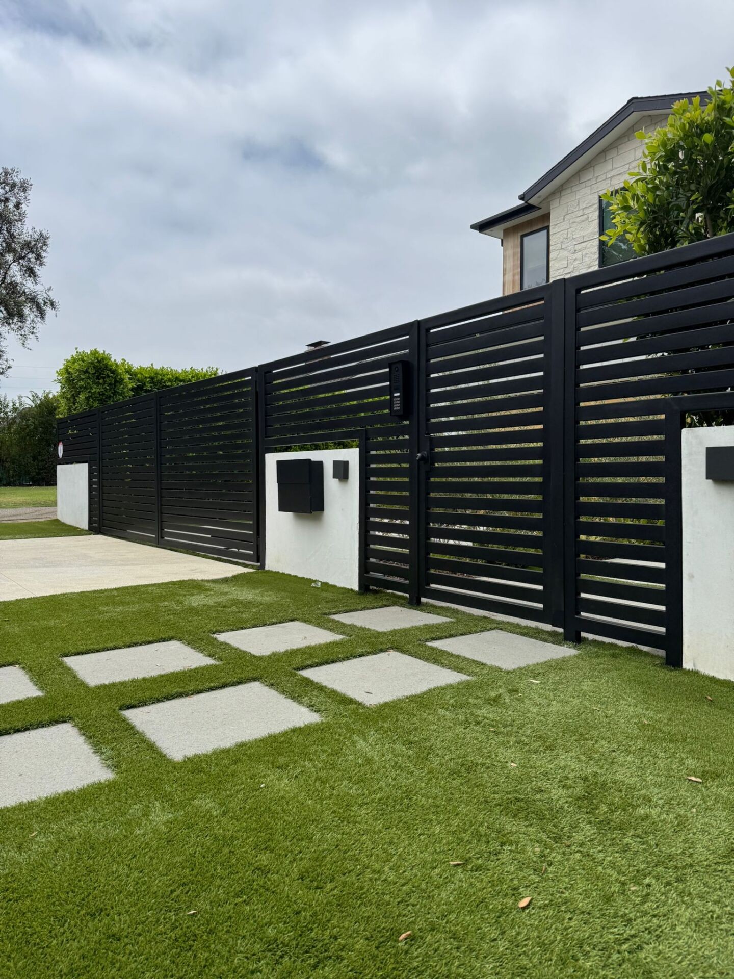 Black horizontal-slat sliding driveway gate with a keypad on the gate post and a mailbox on the pilaster