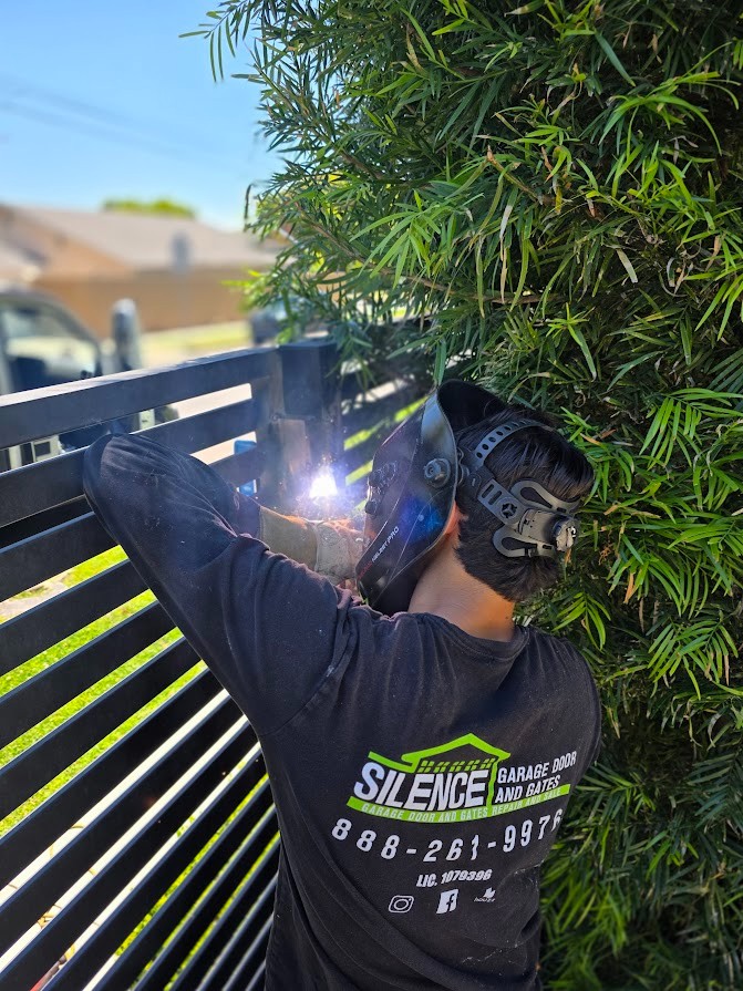 Silence technician in a welding helmet welding a repair on a horizontal-bar driveway gate