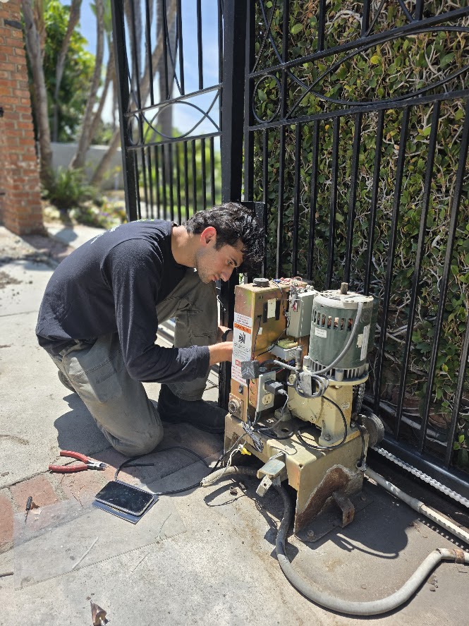 Silence technician servicing a sliding gate operator beside an ornate iron driveway gate
