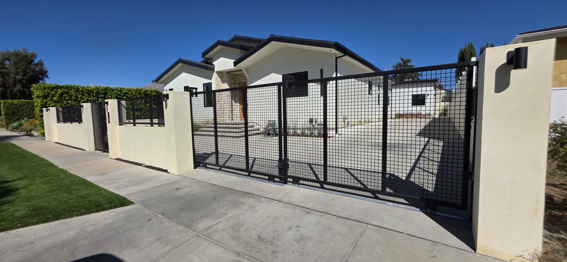 Telescopic sliding driveway gate with lit concrete columns, matching fence and pedestrian gate