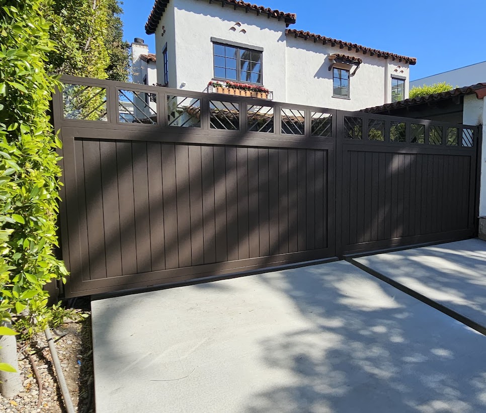 Dark square-top driveway gate with vertical wood infill and a matching pedestrian gate in front of a Spanish-style home