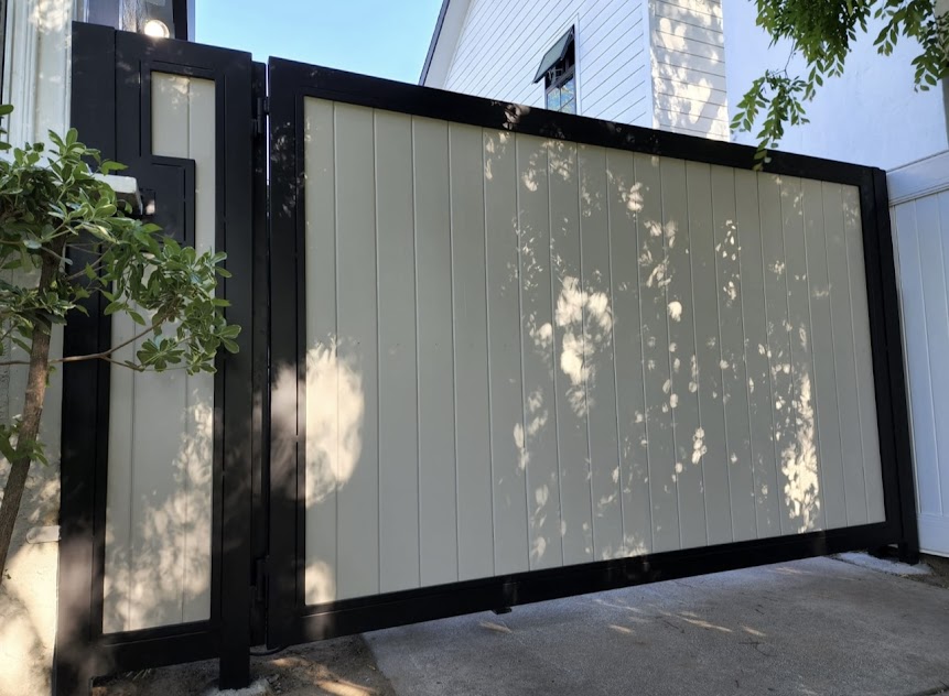Two-tone driveway gate with cream vertical boards set into a black metal frame beside a matching pedestrian gate
